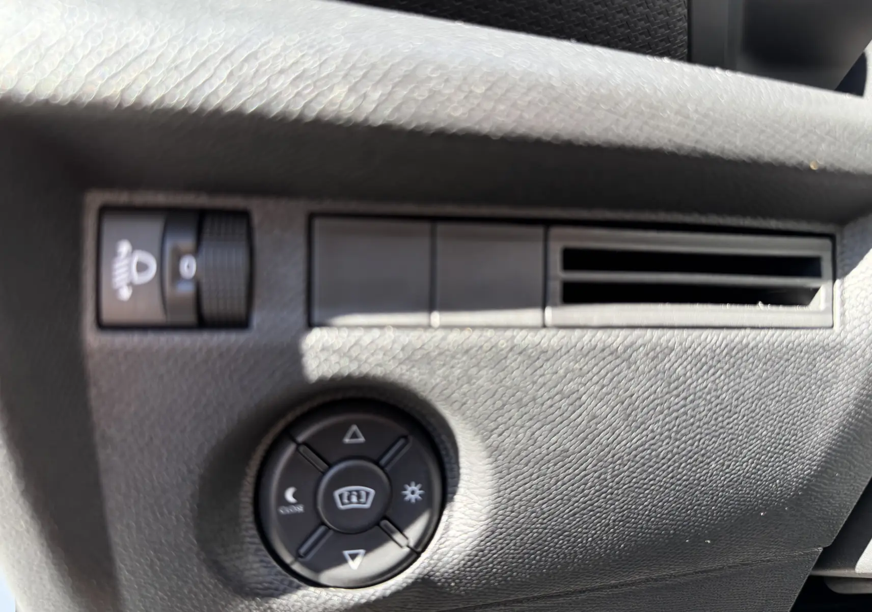 Gros plan sur les commandes d’éclairage et de réglage des rétroviseurs dans l’habitacle noir du Citroën C4 Hybrid 2025.