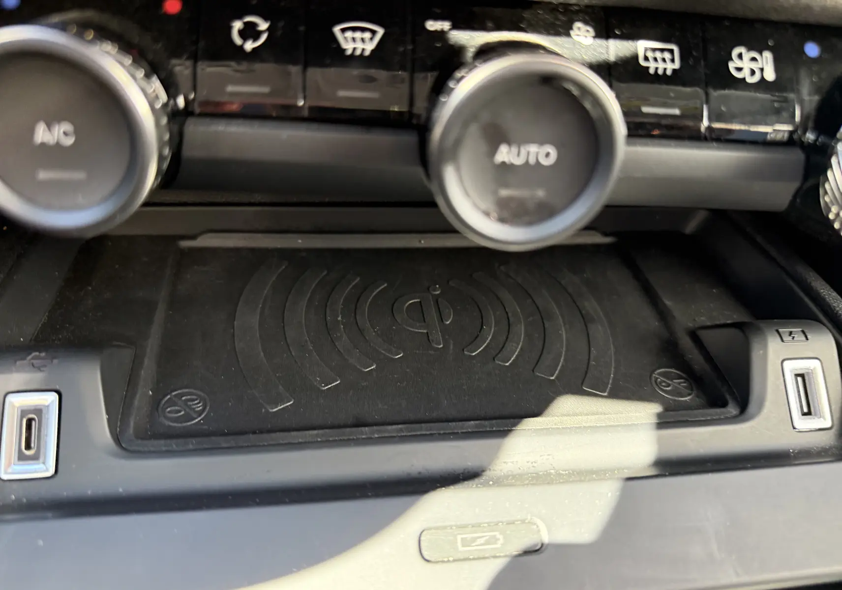 Gros plan sur la zone de recharge sans fil et les commandes de climatisation du Citroën C4 Hybrid 145 CH, intérieur noir.