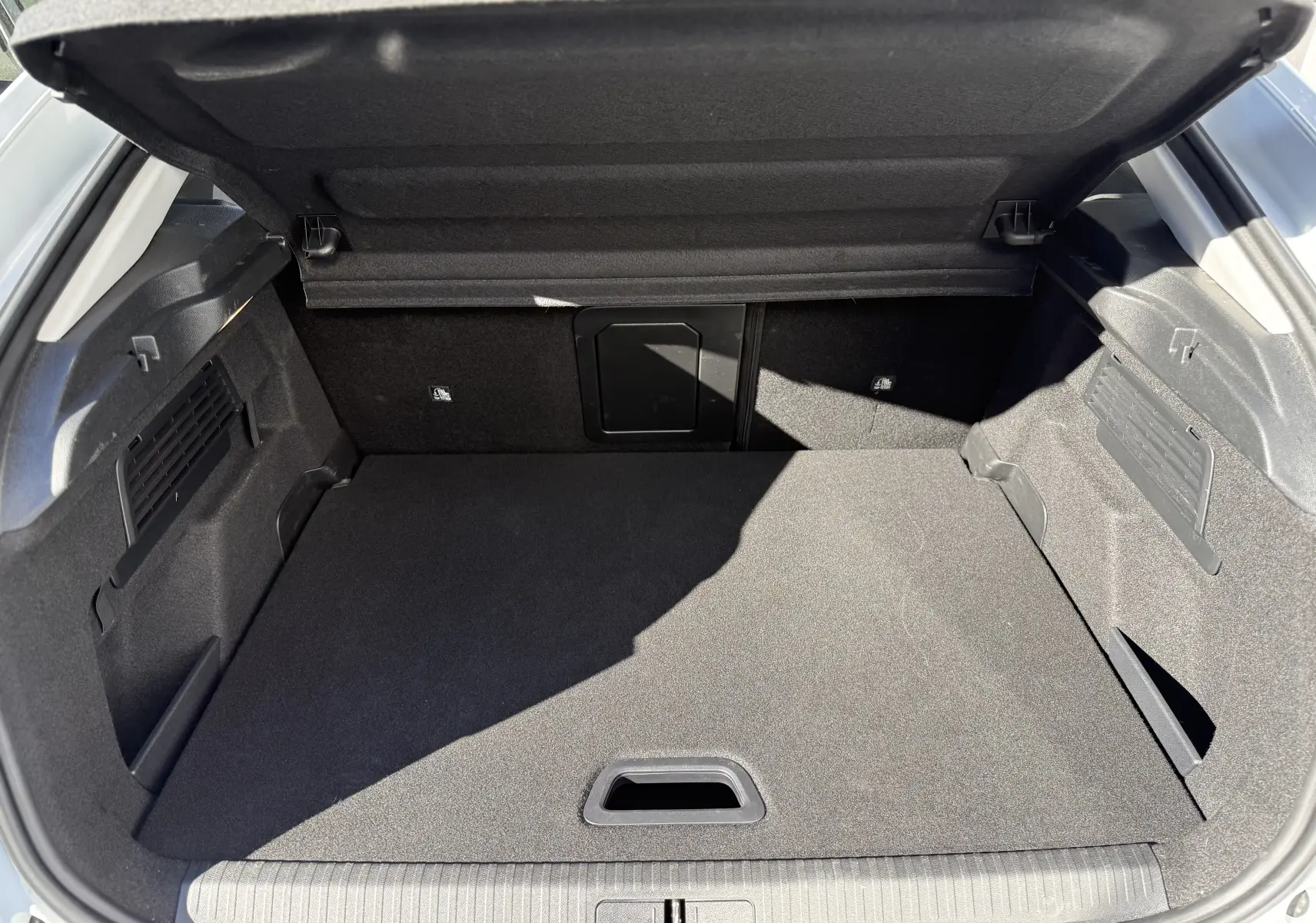 Coffre ouvert vu de l'arrière d'une Citroën C4 Hybrid 145 blanc Okenite, montrant un espace de rangement propre et spacieux.