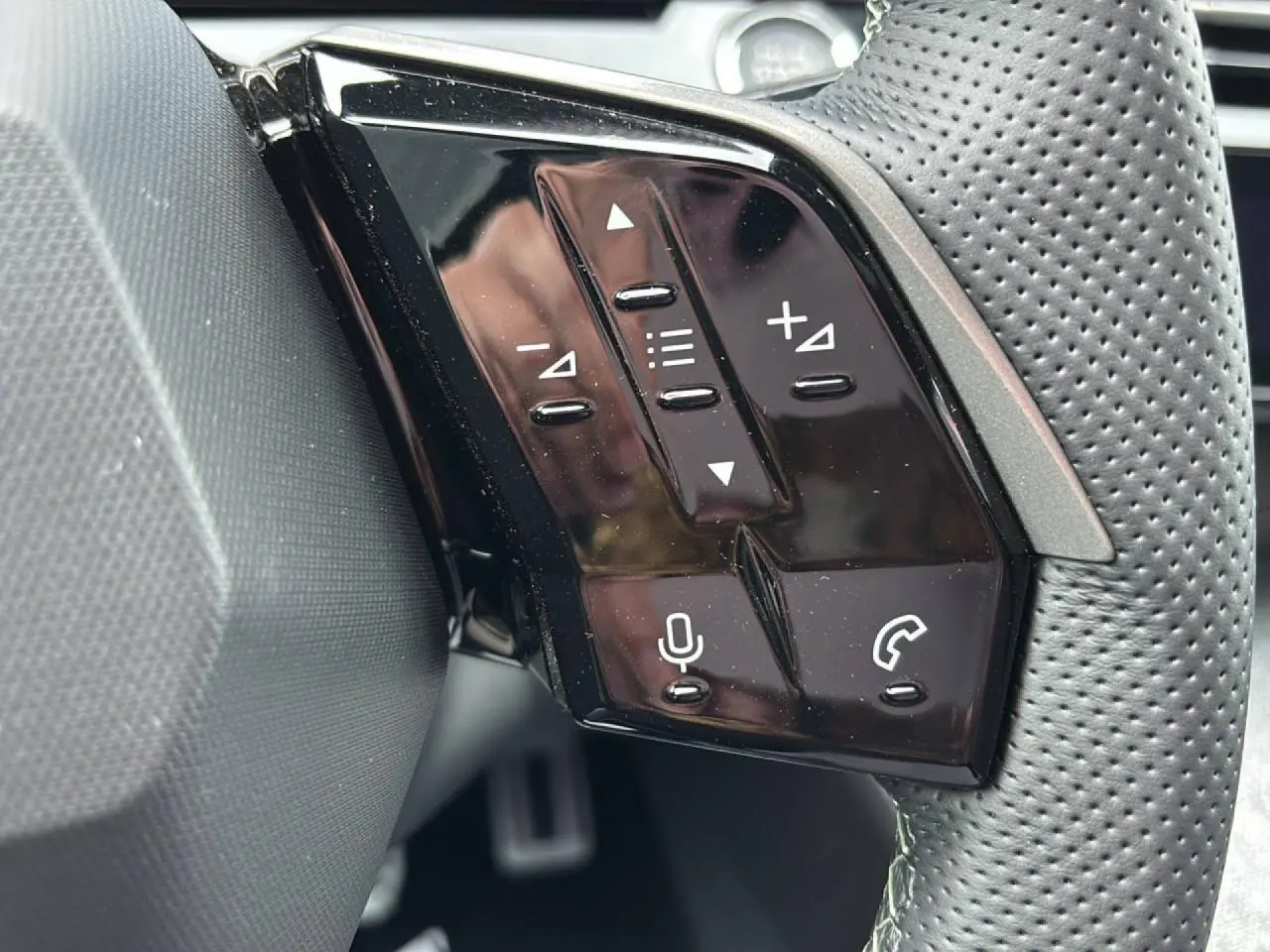 Gros plan sur les commandes noires brillantes du volant perforé du Peugeot 3008 Hybrid 2026.