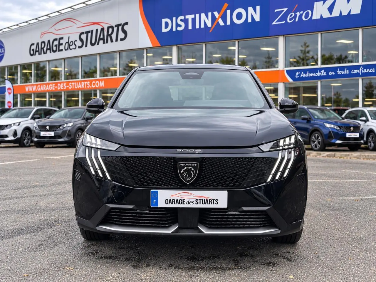 Vue avant d’un Peugeot 3008 noir Perla avec calandre noire et phares LED à griffes distinctives, stationné devant un garage.
