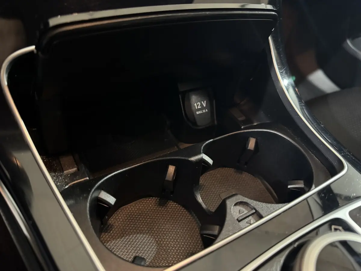 Gros plan sur la console centrale noire du Mercedes Classe C Break C 200 d Business Line avec prise 12V et porte-gobelets.