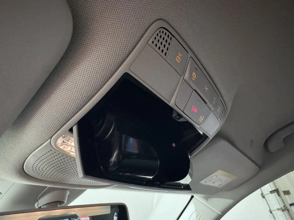 Vue intérieure du plafond d'une Mercedes Classe C Break 2019 noir, avec compartiment lunettes ouvert et commandes éclairage.