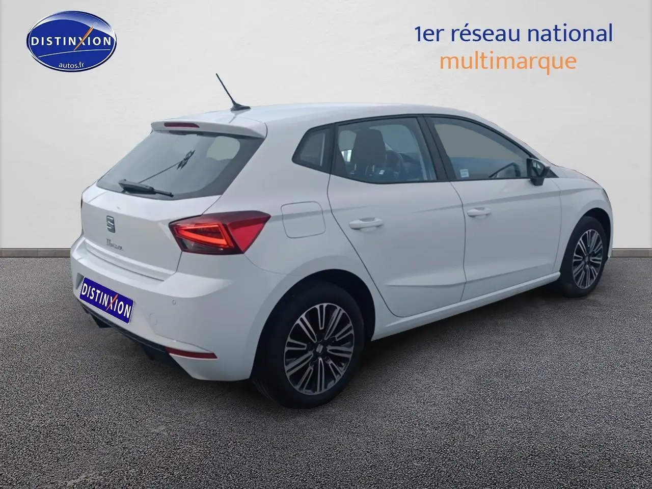 Vue 3/4 arrière droite d'une SEAT Ibiza blanche Nevada avec jantes alliage et feux arrière allumés.