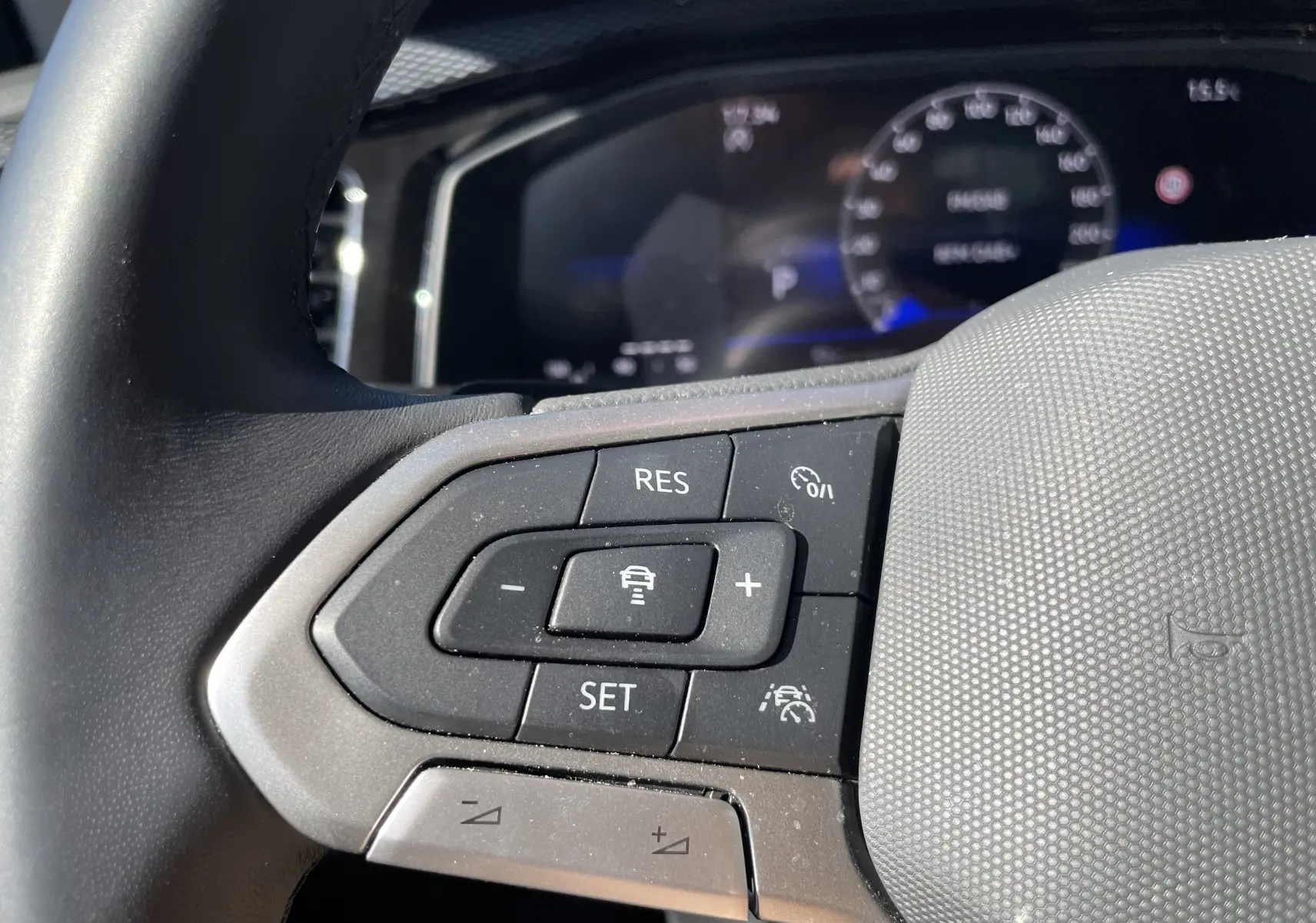 Gros plan sur les commandes au volant côté gauche du Volkswagen Taigo 2024, intérieur gris noir avec boutons de régulateur de vitesse.