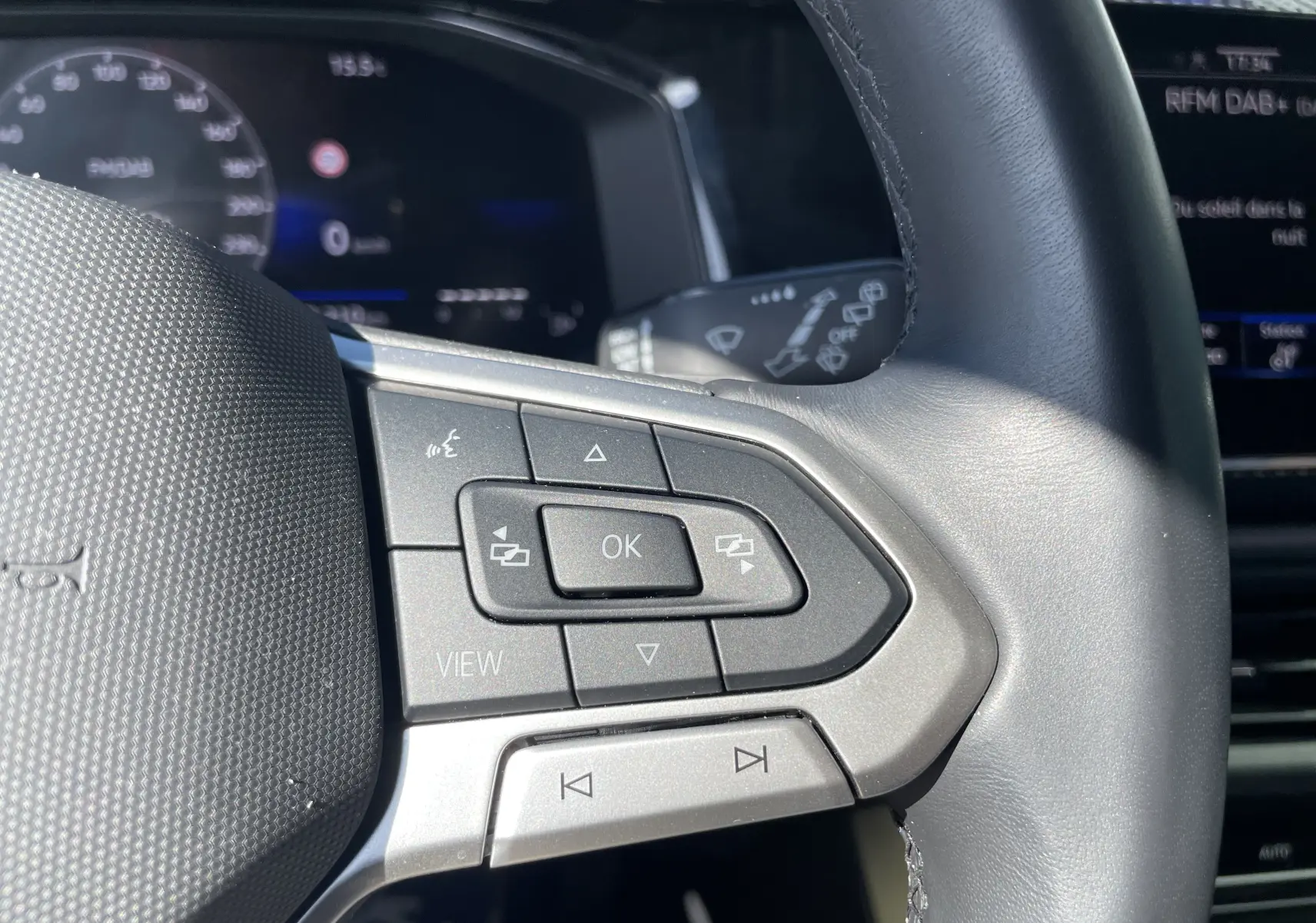 Gros plan sur les commandes multifonctions à droite du volant cuir gris-noir du Volkswagen Taigo rouge Roi 2024.