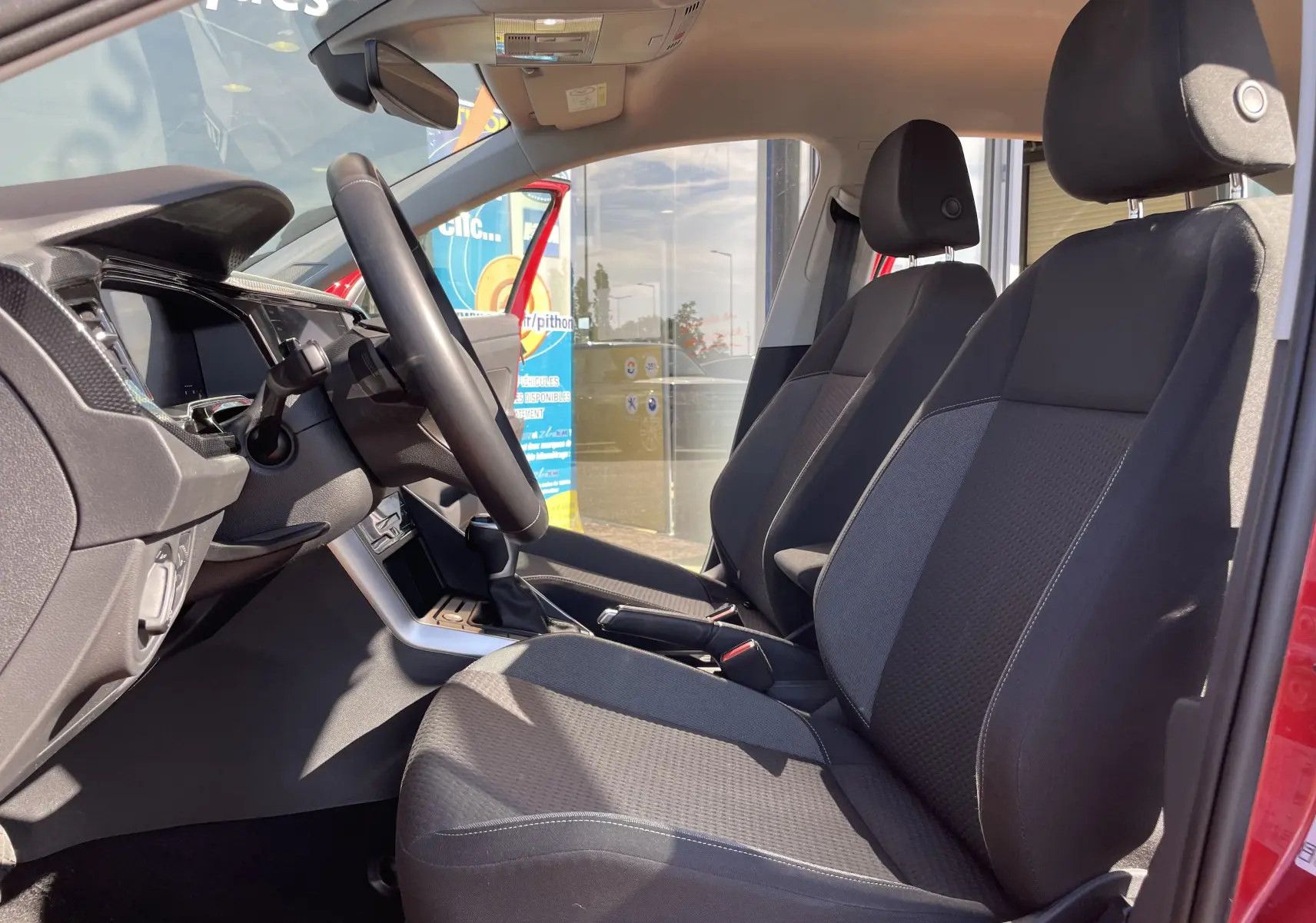 Vue intérieure côté conducteur du Volkswagen Taigo 2024 rouge Roi, sièges tissu gris noir et volant cuir.