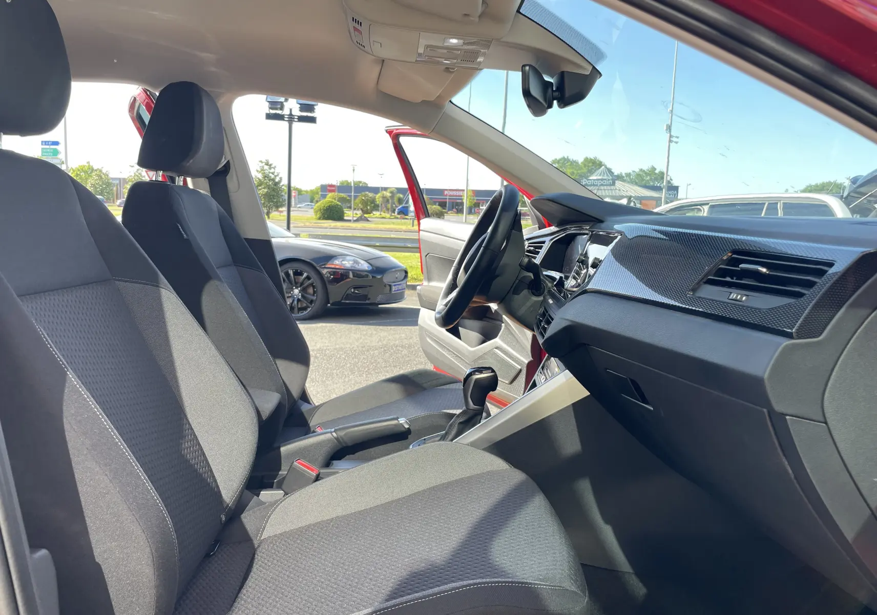 Vue intérieure côté conducteur du Volkswagen Taigo rouge Roi 2024, montrant les sièges gris et le tableau de bord moderne.