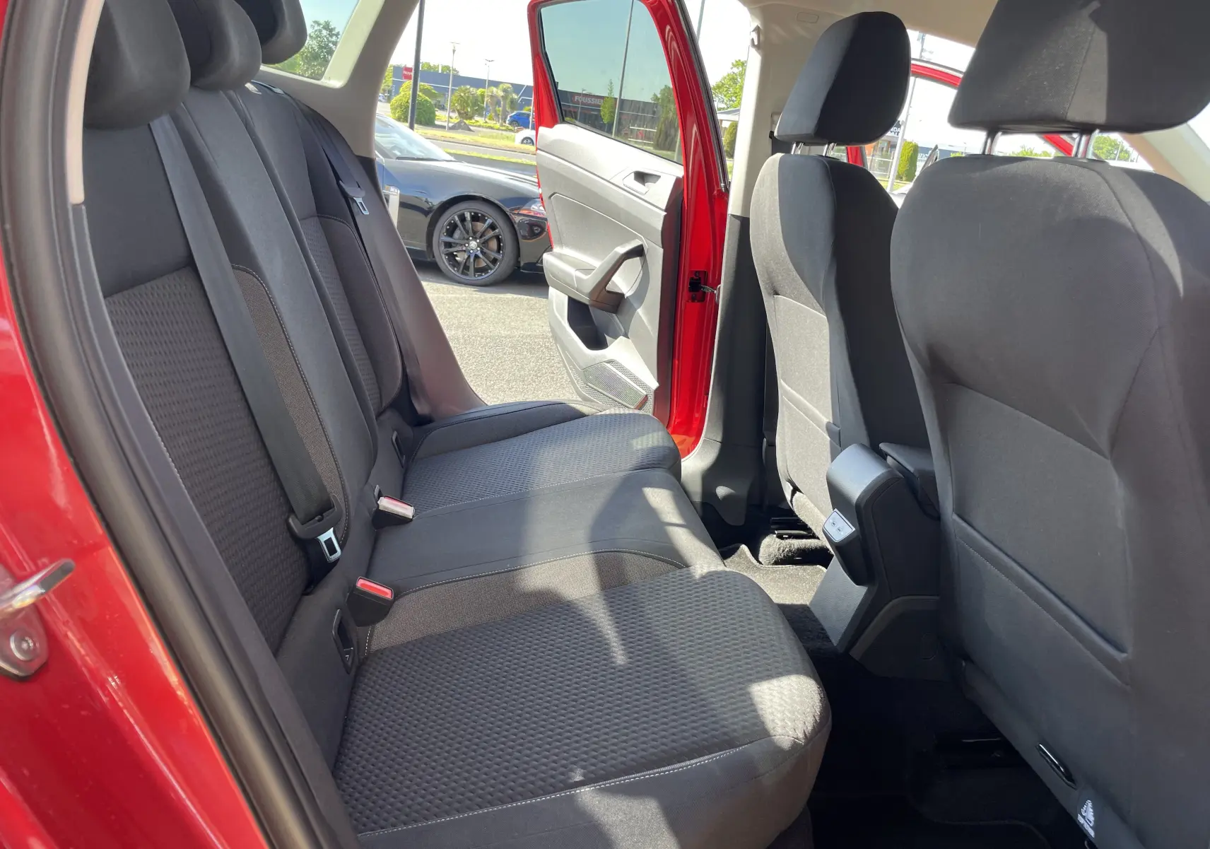 Vue intérieure arrière côté gauche du Volkswagen Taigo rouge roi 2024, montrant les sièges arrière en tissu gris foncé.