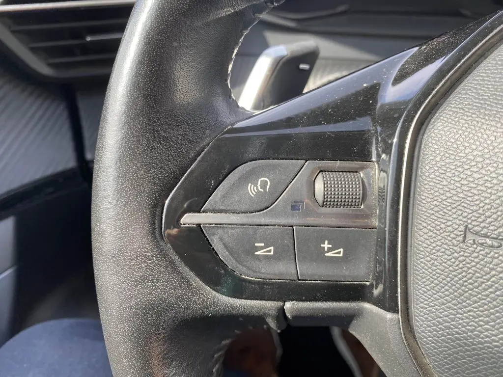 Gros plan sur les commandes de volume et téléphone au volant noir du Peugeot 2008 gris clair, version 2020.