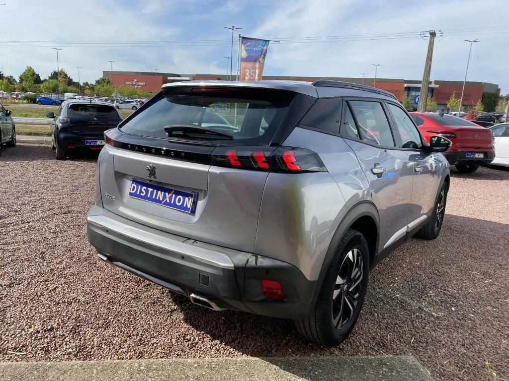 Vue 3/4 arrière droite d'un Peugeot 2008 gris clair avec barres de toit noires et feux arrière LED distinctifs.
