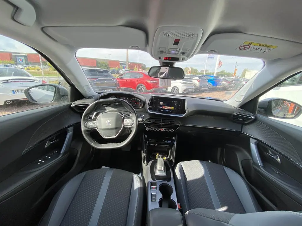 Vue intérieure avant de la Peugeot 2008 gris clair, montrant le tableau de bord, le volant et l’écran tactile central.