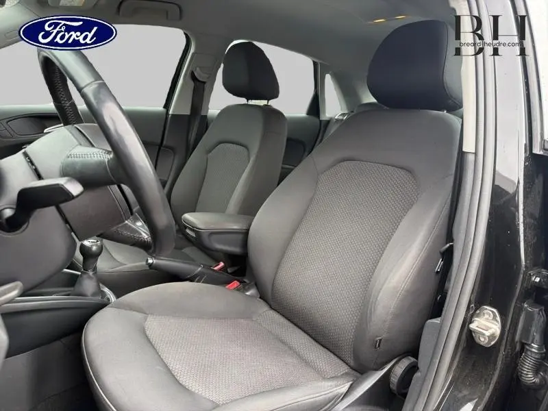 Vue intérieure côté conducteur de l'Audi A1 Sportback noire, sièges tissu gris et volant cuir multifonction.