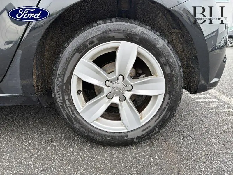 Gros plan sur la roue avant droite d'une Audi A1 Sportback noire brillante avec jante alu cinq branches.