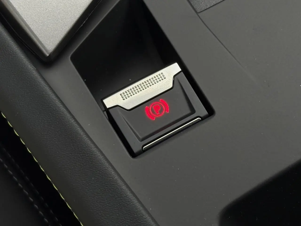 Gros plan sur le bouton de frein de parking électrique illuminé en rouge dans l'habitacle noir du Peugeot 308 SW Hybrid.
