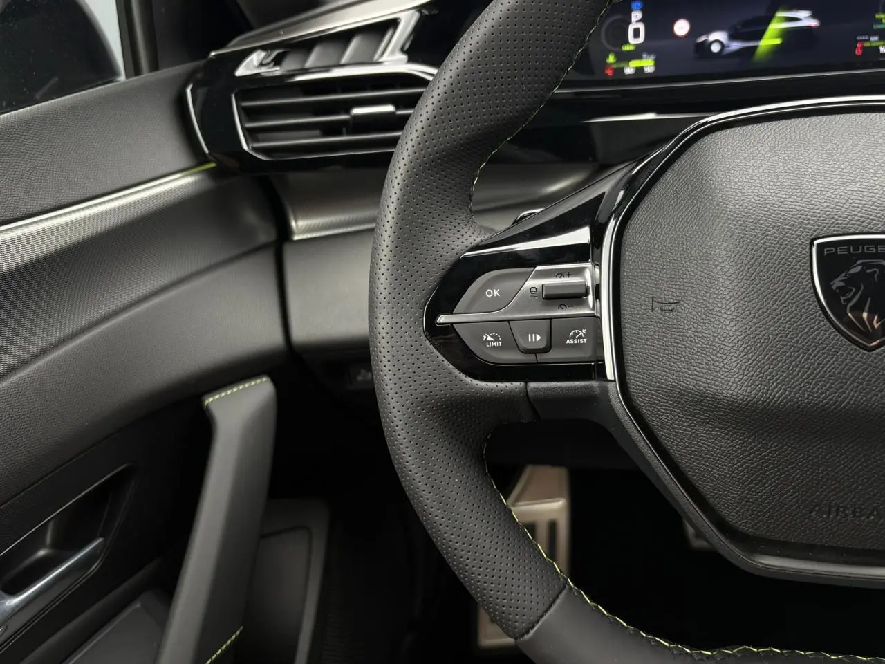 Gros plan sur le volant perforé noir avec surpiqûres vert Adamite et partie gauche du tableau de bord gris foncé.