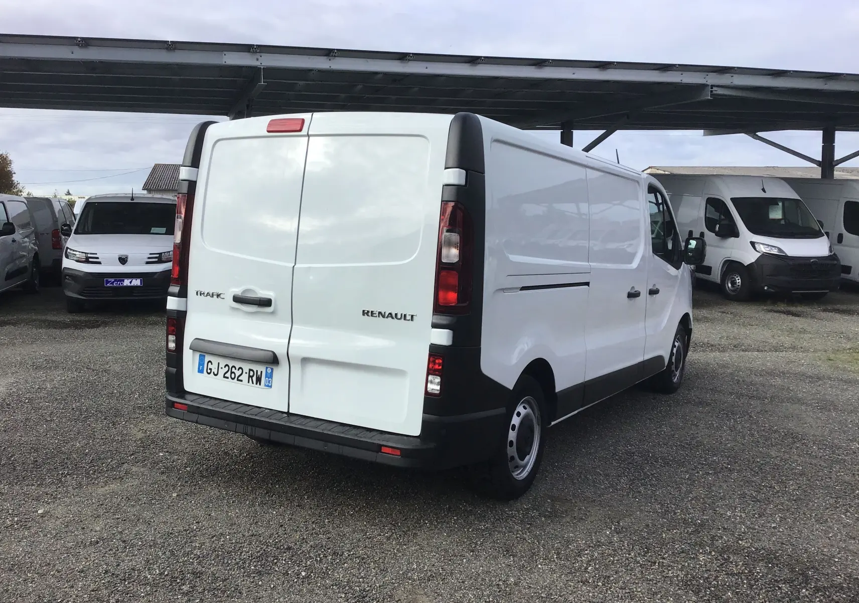 Renault Trafic Fourgon blanc vu de l'arrière côté gauche, avec portes arrière fermées et feux verticaux noirs.