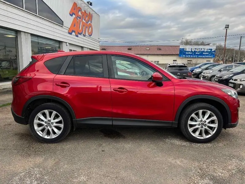 Vue de profil côté gauche d'un Mazda CX-5 2013 Soul Red Métallisé avec jantes alu 19 pouces sur parking extérieur.