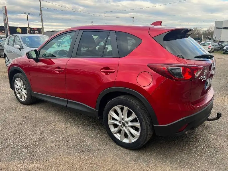 Vue 3/4 arrière droit d'un Mazda CX-5 2013 Soul Red Métallisé avec jantes alu et attelage visible.