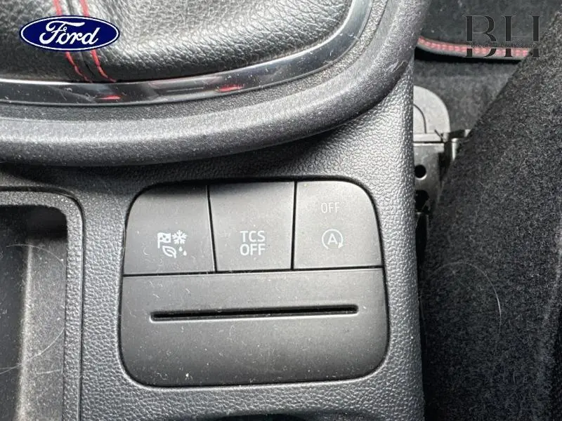 Gros plan sur les commandes situées devant le levier de vitesse cuir, avec surpiqûres rouges visibles du volant sport.