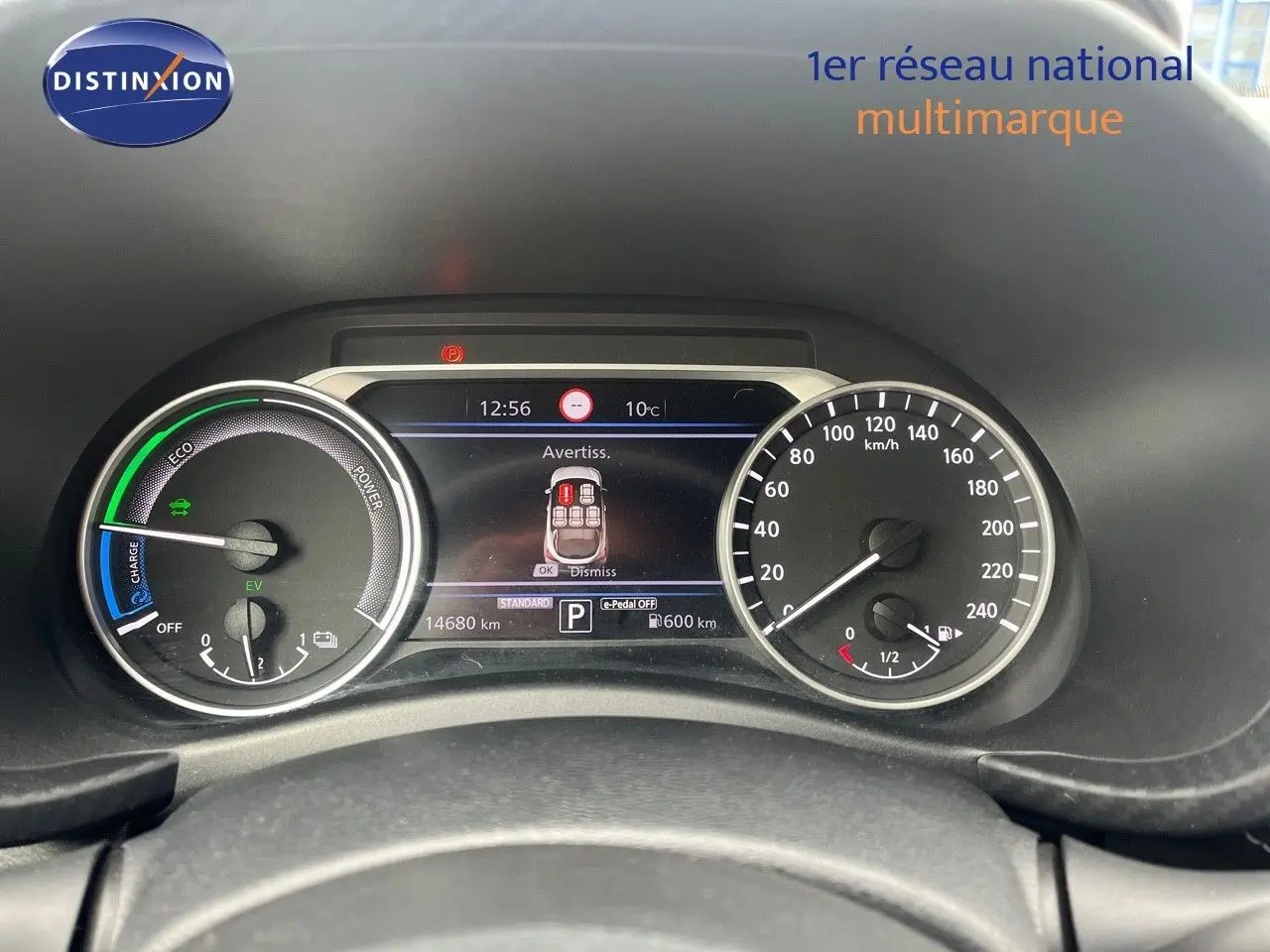 Vue rapprochée du tableau de bord du Nissan Juke blanc nacré 2024, affichant les compteurs hybrides et l'écran central.