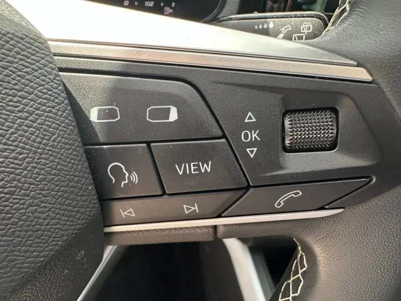 Gros plan sur les commandes noires du volant cuir multifonction du SEAT Arona 2025 blanc Candy avec détails en surpiqûres blanches.