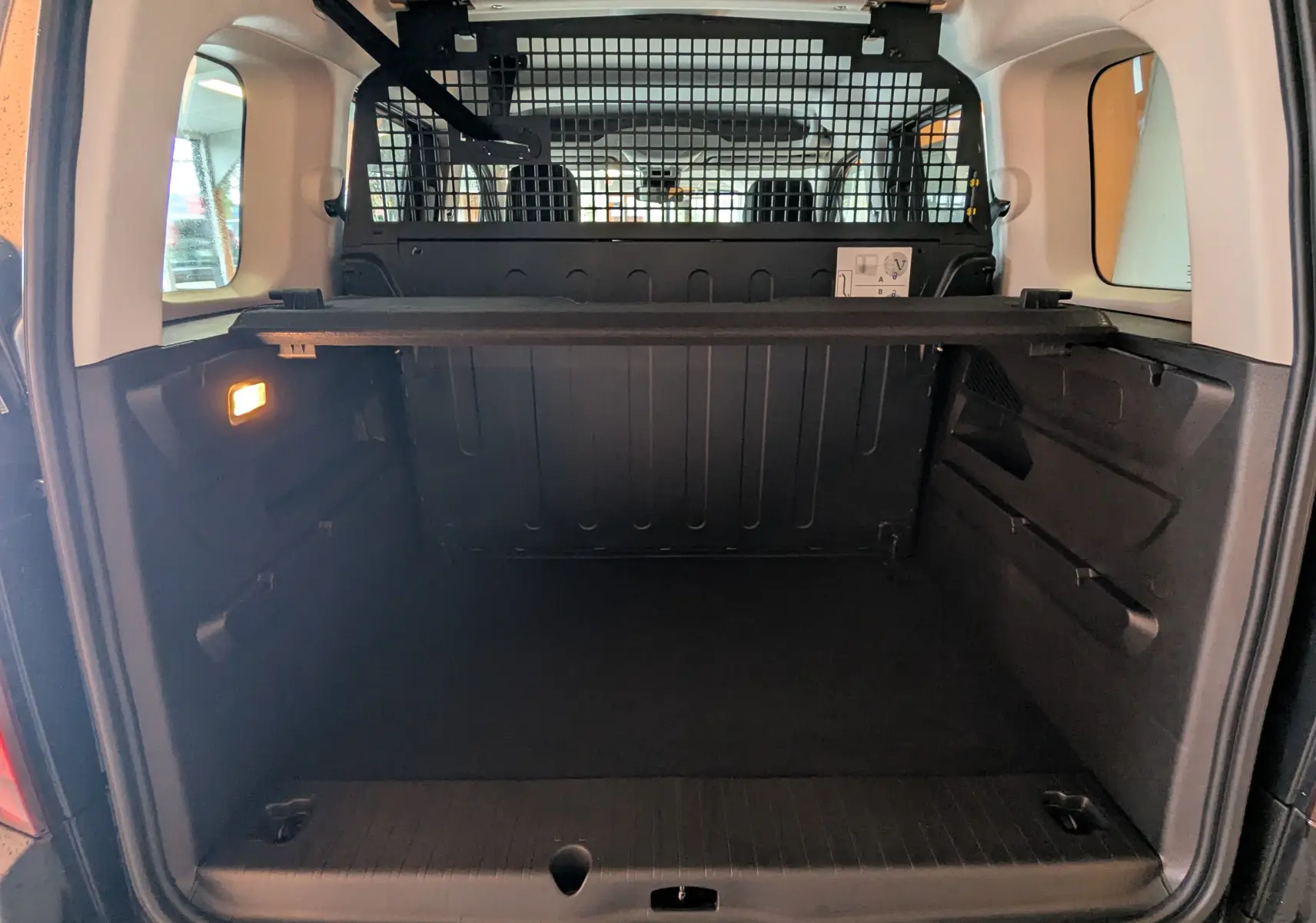 Vue arrière du coffre spacieux du Peugeot Rifter gris Artense 2025 avec séparation grillagée et tablette de rangement.