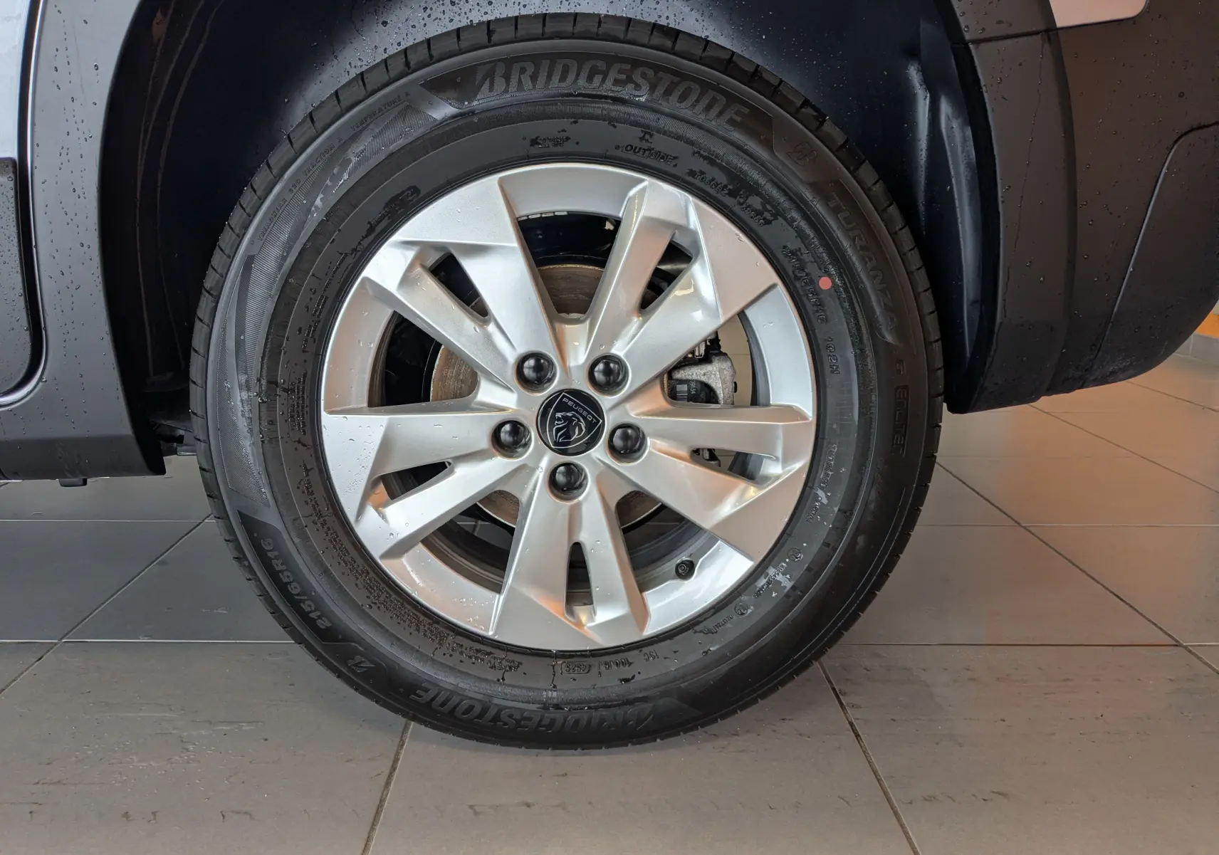 Gros plan sur la roue avant droite du Peugeot Rifter gris Artense 2025 avec jante alliage 16 pouces et logo lion central.