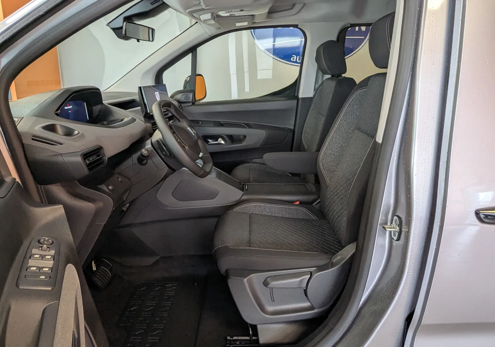 Vue intérieure côté conducteur du Peugeot Rifter gris Artense 2025, montrant les sièges tissu et le tableau de bord moderne.