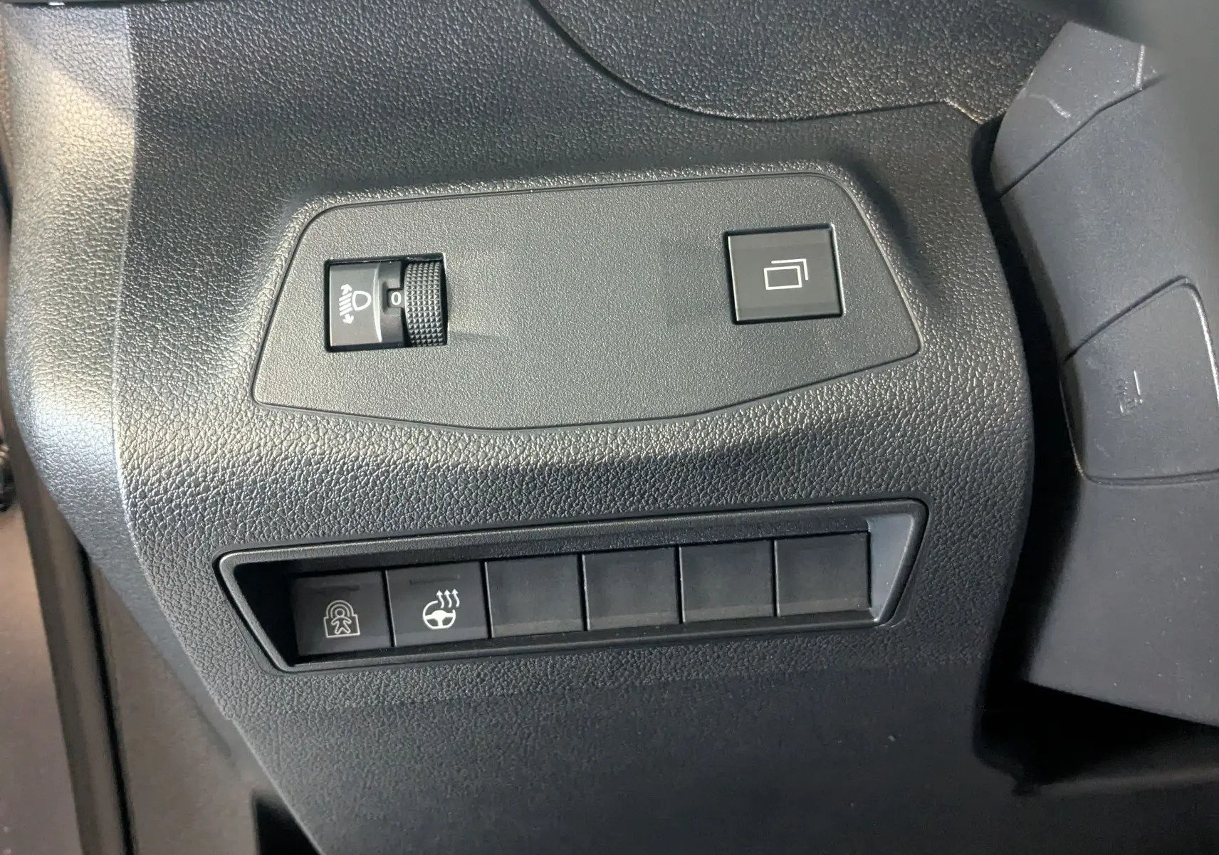 Vue rapprochée des commandes noires sur tableau de bord du Peugeot Rifter gris Artense, incluant réglage phares et siège chauffant.