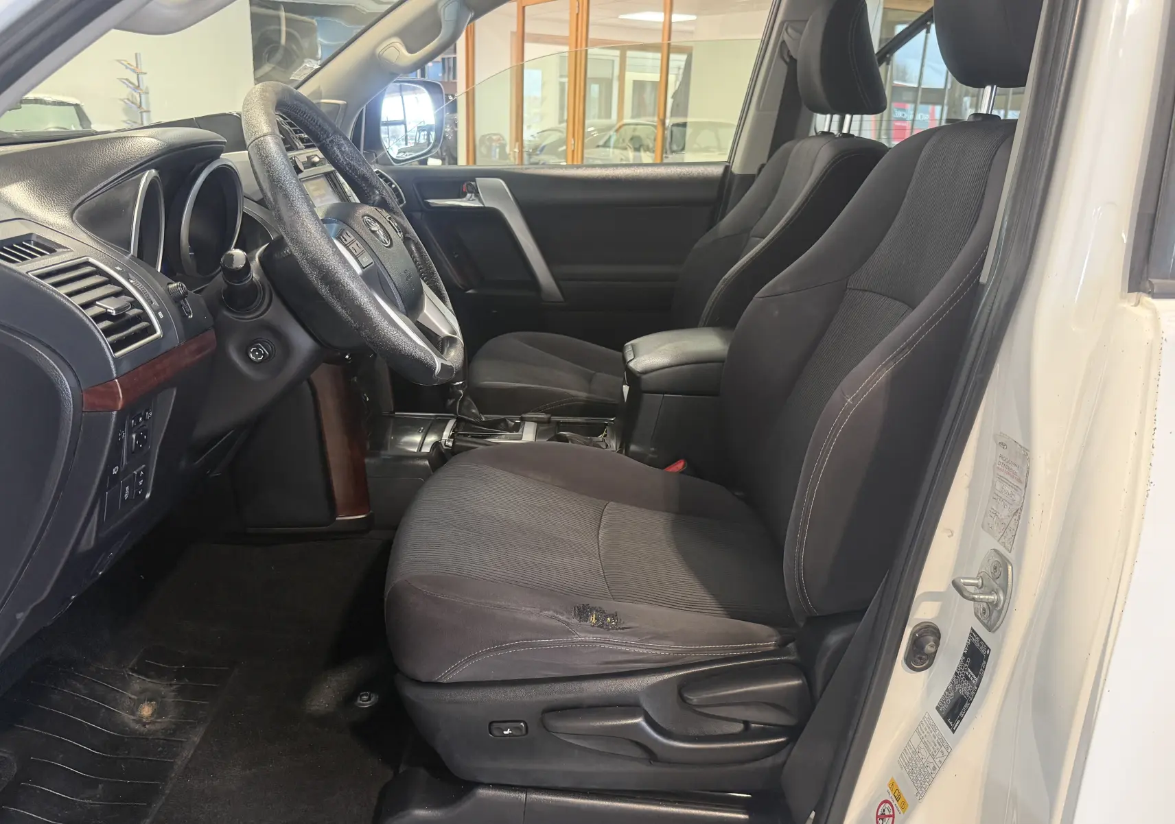 Vue intérieure côté gauche du Toyota Land Cruiser blanc 2015, montrant les sièges avant noirs et le tableau de bord.