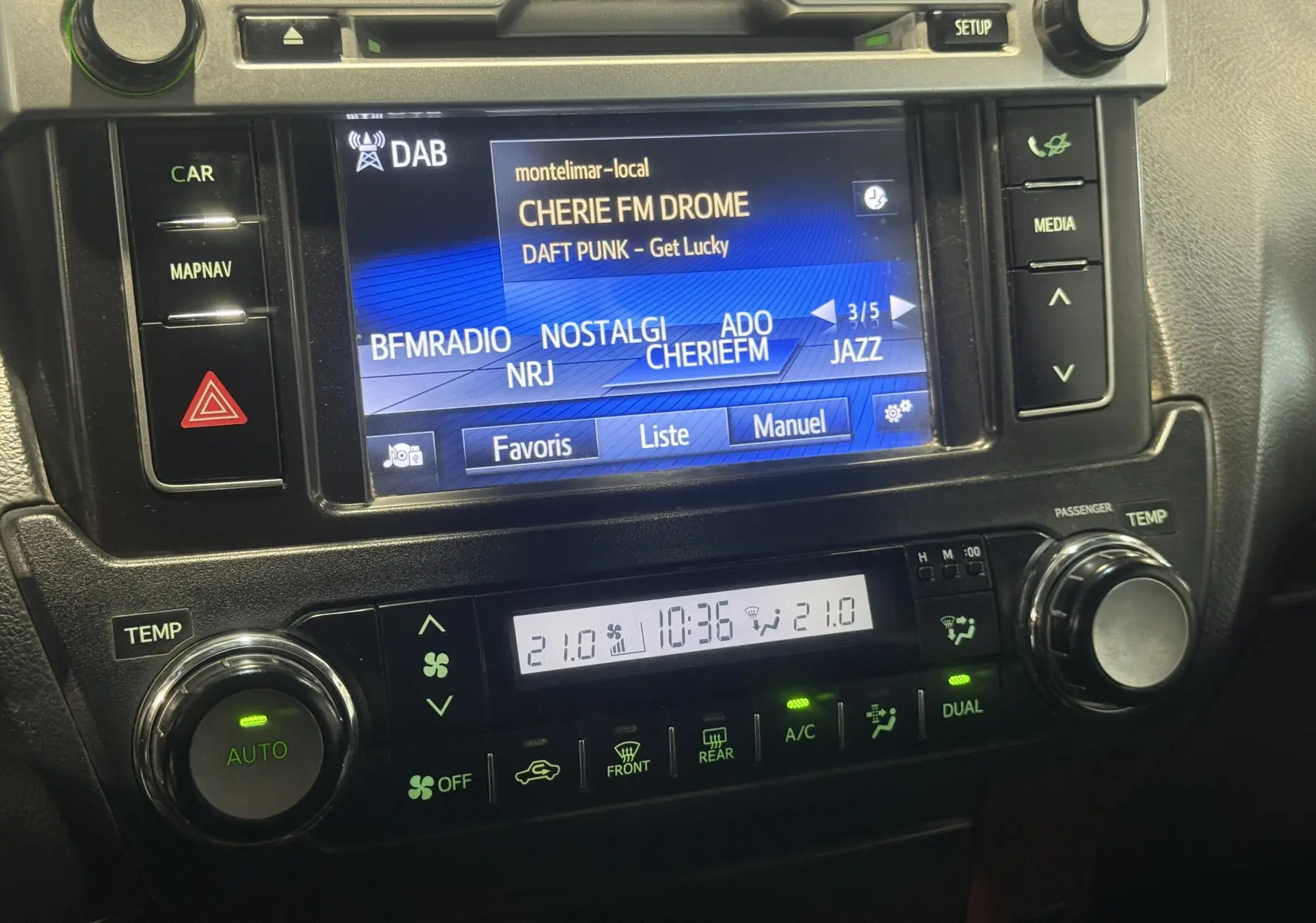 Gros plan sur l’écran multimédia et la console de climatisation du Toyota Land Cruiser blanc, affichant une radio DAB et la température à 21°C.