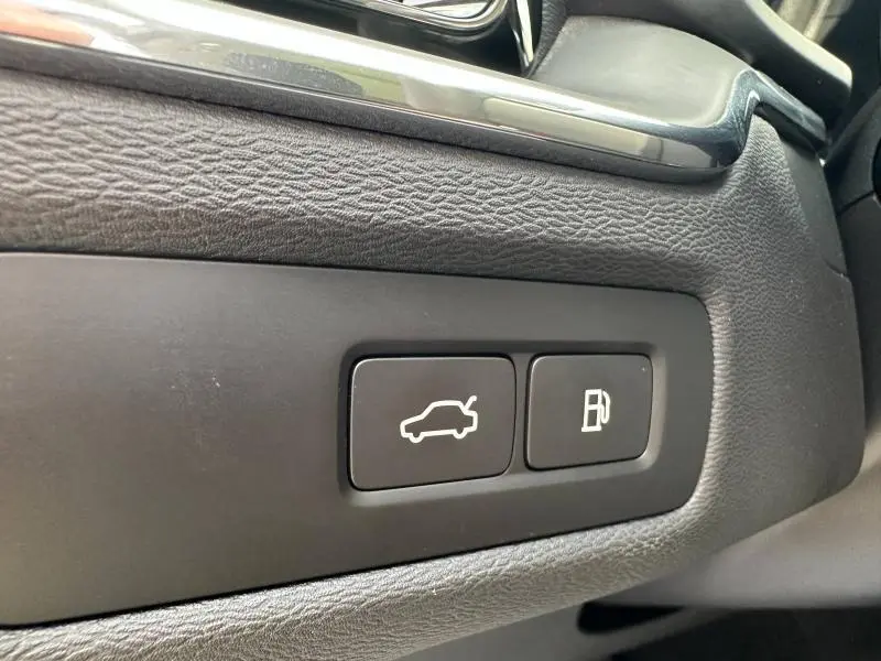 Boutons d'ouverture du coffre et de la trappe à carburant sur la planche de bord noire d'un Volvo XC60 blanc.