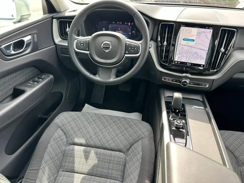 Vue intérieure avant du Volvo XC60 2024, volant cuir multifonction, écran tactile vertical et sièges tissu gris à motifs.