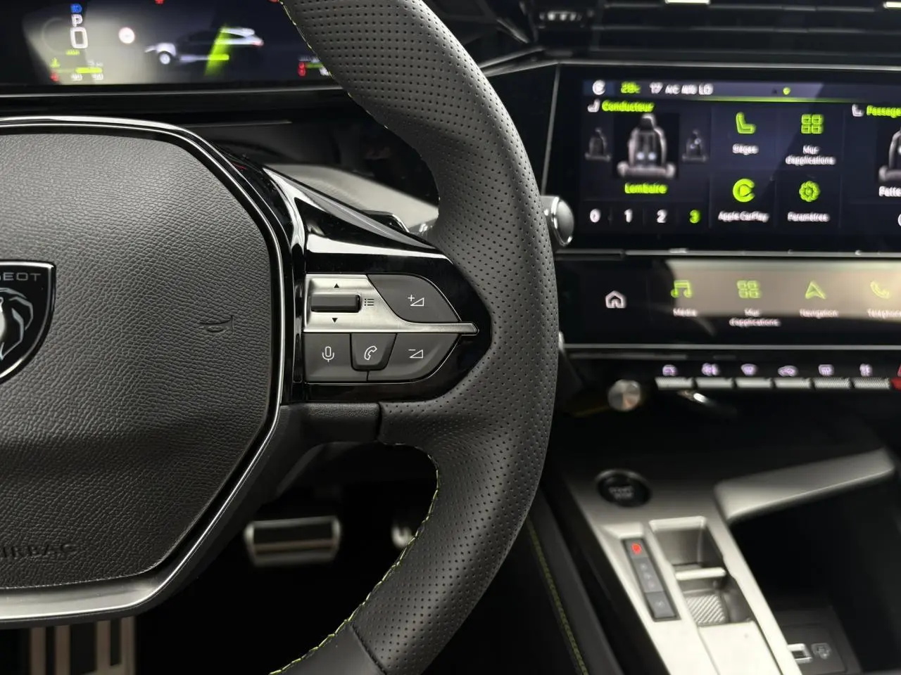 Intérieur de la Peugeot 308 SW Hybrid 2026, vue rapprochée du volant perforé noir avec surpiqûres vertes et écran tactile.
