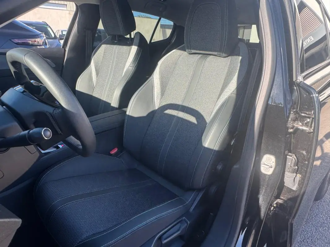Vue intérieure côté conducteur de la Peugeot 408 Hybrid 145 Allure 2025 noire, mettant en valeur les sièges en tissu et cuir.