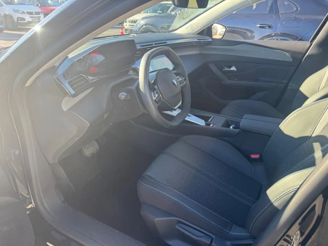 Vue intérieure côté conducteur du Peugeot 408 Hybrid 145 e-DCS6 Allure 2025, sièges noirs et tableau de bord moderne.