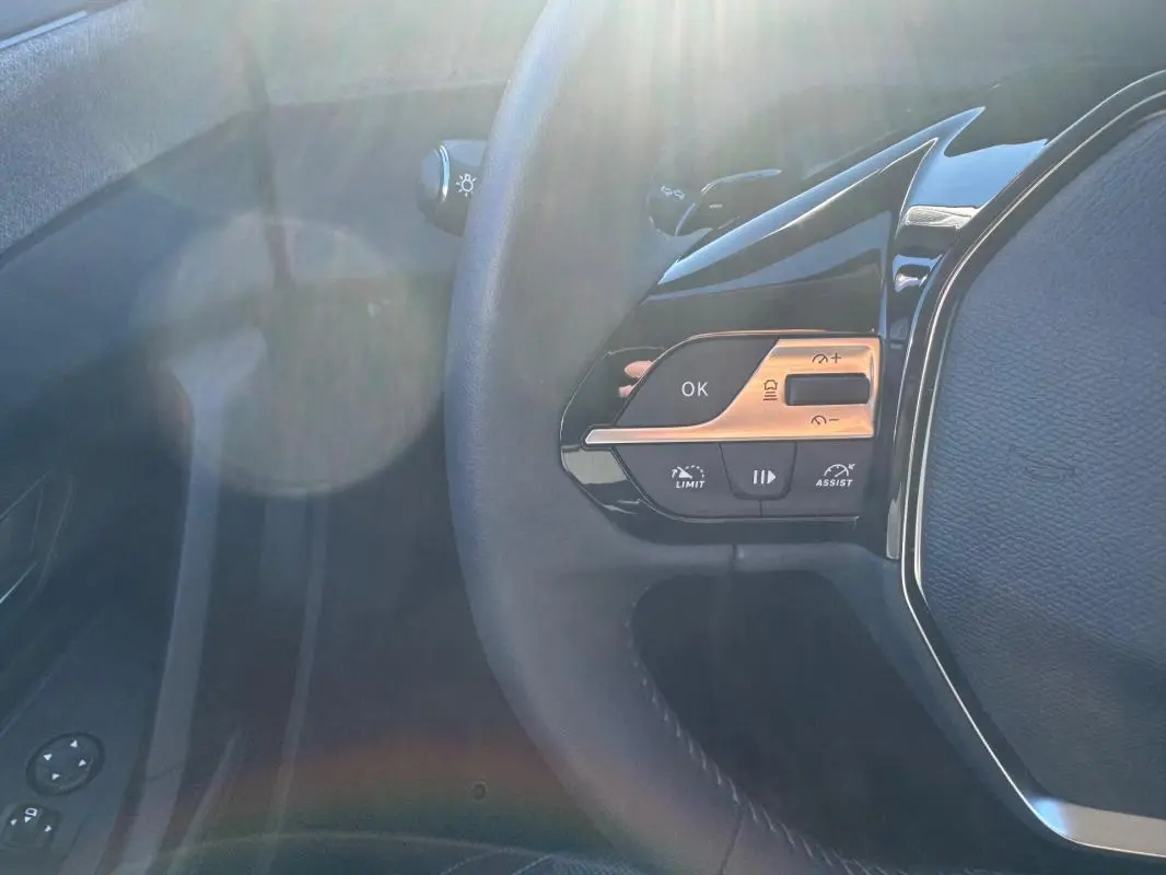 Gros plan sur les commandes à gauche du volant noir du Peugeot 408 Hybrid 145 e-DCS6 Allure 2025, avec boutons multifonctions.
