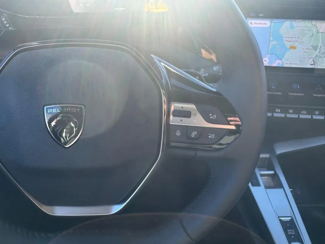 Vue rapprochée du volant noir de la Peugeot 408 Hybrid 145 e-DCS6 Allure 2025 avec commandes intégrées et écran tactile visible.