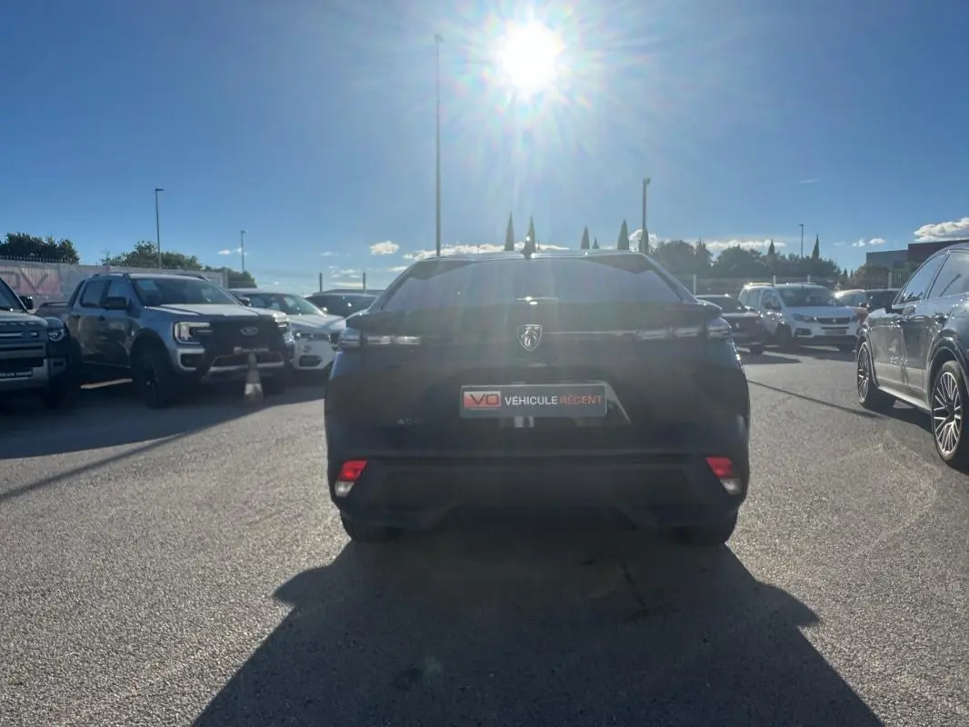 Vue arrière d'une Peugeot 408 Hybrid 145 e-DCS6 Allure noire 2025, stationnée en extérieur sous un soleil éclatant.