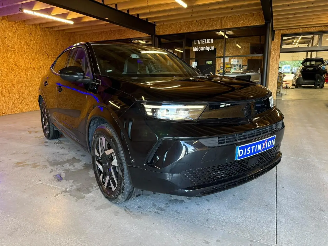 Opel Mokka noir vue 3/4 avant droit, calandre Vizor noire et jantes alliage 17'' diamantées, en intérieur d'atelier.
