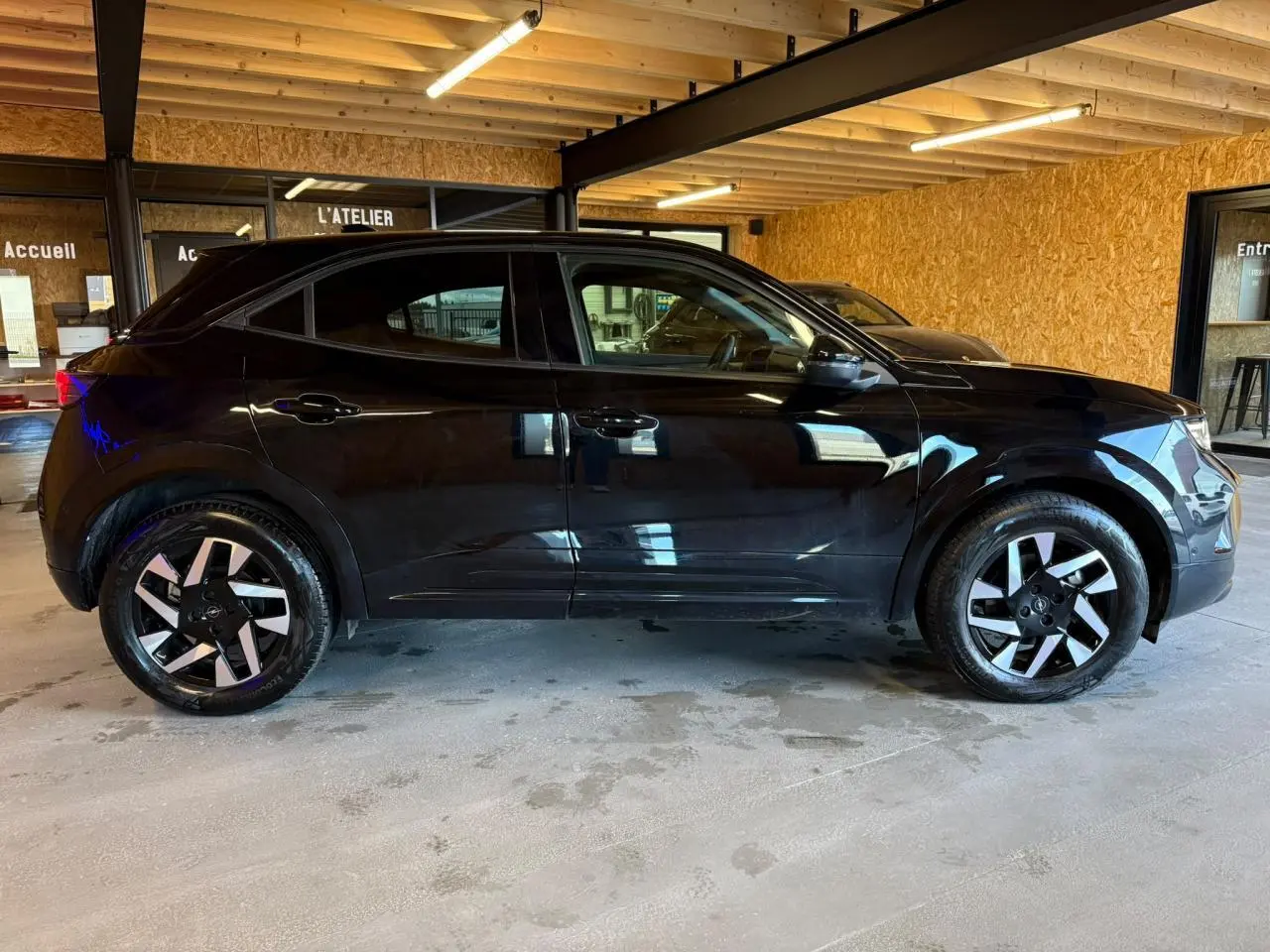Opel Mokka noir vue de profil côté gauche, avec jantes alliage diamantées et vitres surteintées en intérieur d'atelier.