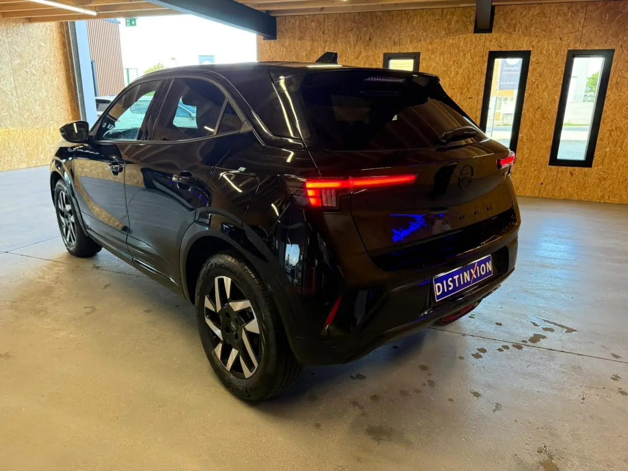 Opel Mokka noir vue 3/4 arrière droit en intérieur, feux arrière LED allumés et jantes alliage 17 pouces.