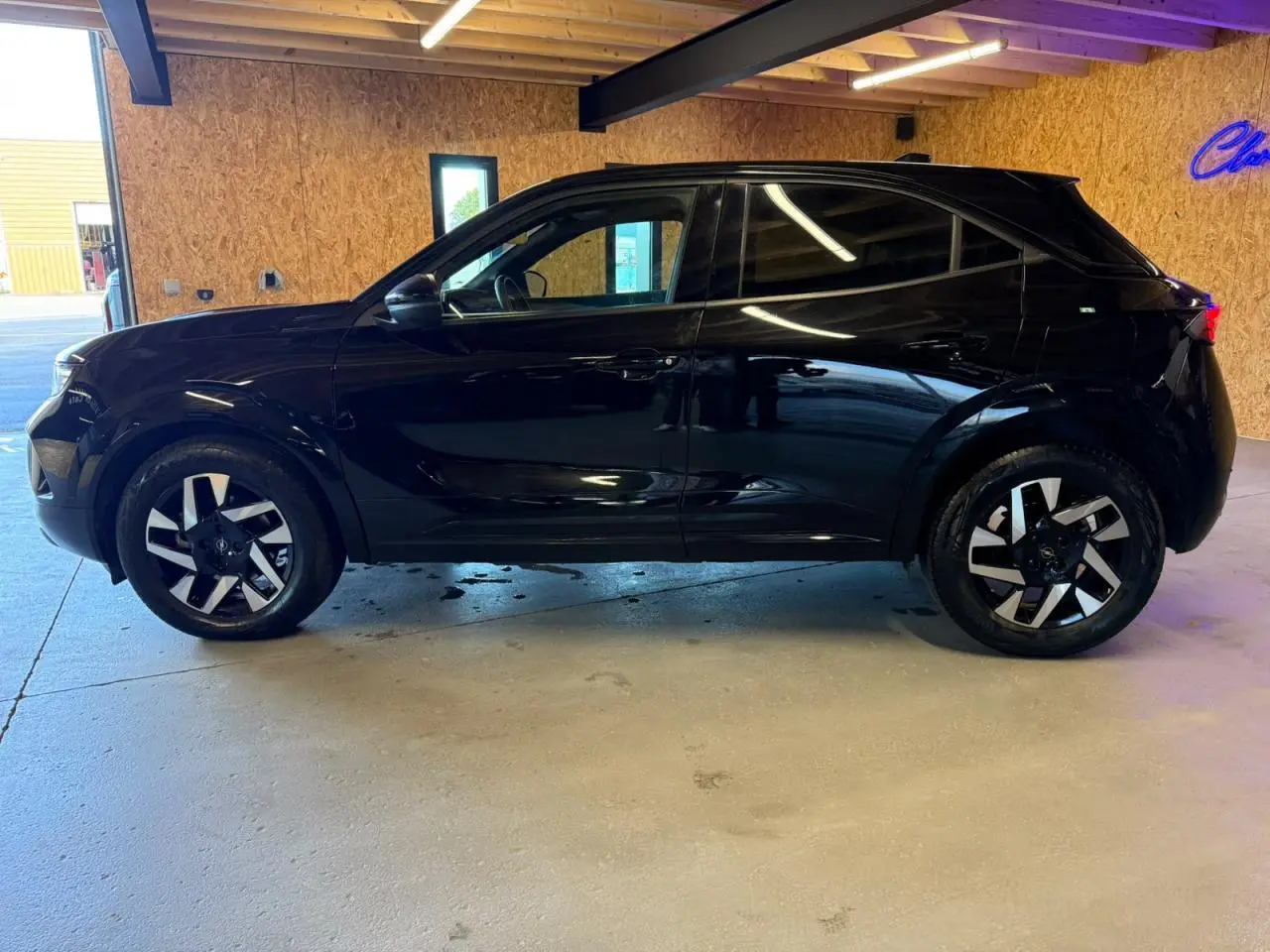 Profil côté gauche d’un Opel Mokka noir métallisé 2025 avec jantes alliage 17 pouces diamantées, garé en intérieur.
