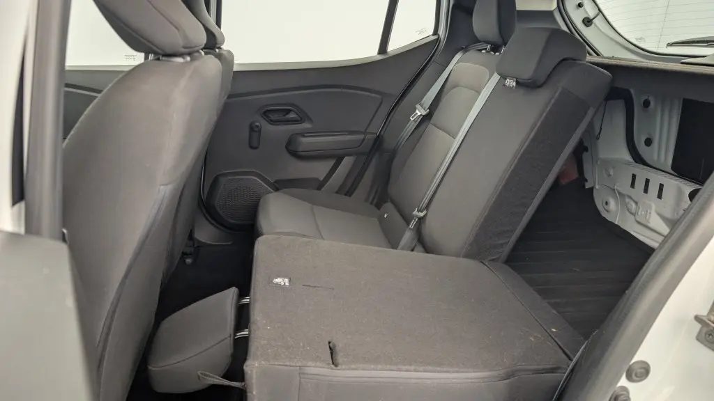 Vue intérieure côté droit de la banquette arrière rabattue en partie d'une Dacia Sandero blanche, soulignant l'espace de chargement.