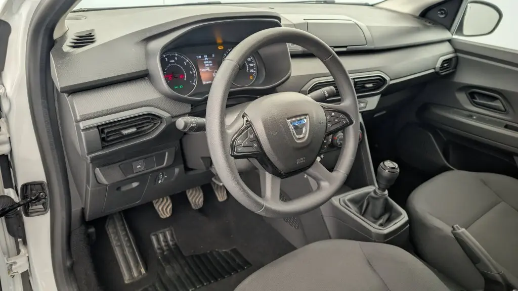 Vue intérieure côté conducteur de la Dacia Sandero blanche 2022, volant mousse et tableau de bord avec écran TFT.
