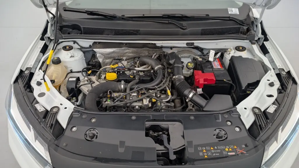 Vue plongeante sur le moteur de la Dacia Sandero blanc glacier 2022 avec capot ouvert et détails du compartiment moteur visible.