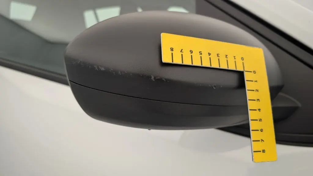 Gros plan sur le rétroviseur côté gauche noir mat de la Dacia Sandero blanche 2022 avec rayures visibles.