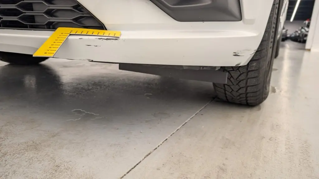 Gros plan sur l'angle avant droit d'une Dacia Sandero blanche avec rayures visibles sur le pare-chocs inférieur.