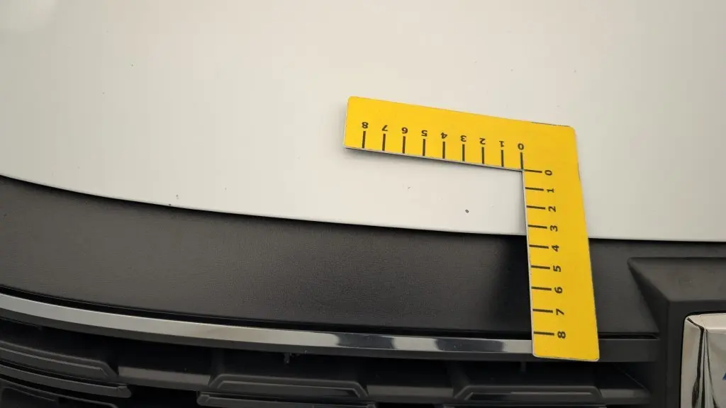 Gros plan sur le capot blanc glacier et la calandre noire d'une Dacia Sandero Eco-G 100 2022 avec un outil de mesure jaune posé dessus.